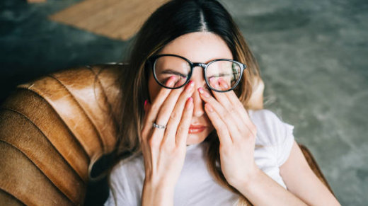 Young woman rubs her eyes after using glasses. Eye pain or fatigue concept.